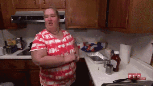 a woman in a red and white shirt is standing in a messy kitchen ..
