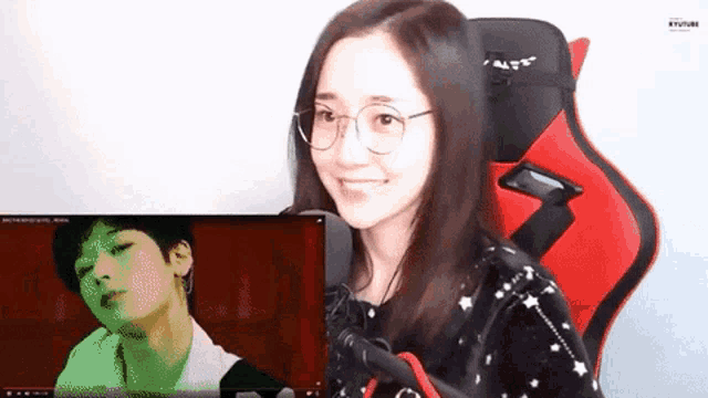 a woman wearing glasses is sitting in a red chair and watching a video