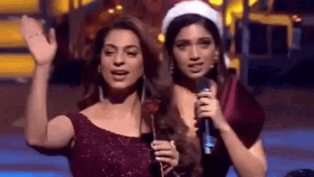 two women are standing next to each other on a stage and holding microphones .