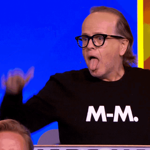 a man wearing glasses and a shirt that says m-m sticking out his tongue