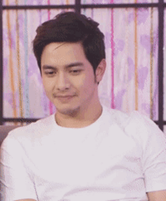 a man wearing a white t-shirt is sitting in front of a striped curtain