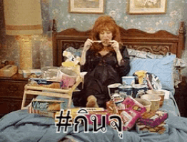 a woman is sitting on a bed with a tray of food and the word # written on it