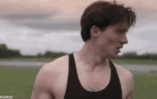 a man in a black tank top is standing in a field looking at the camera .