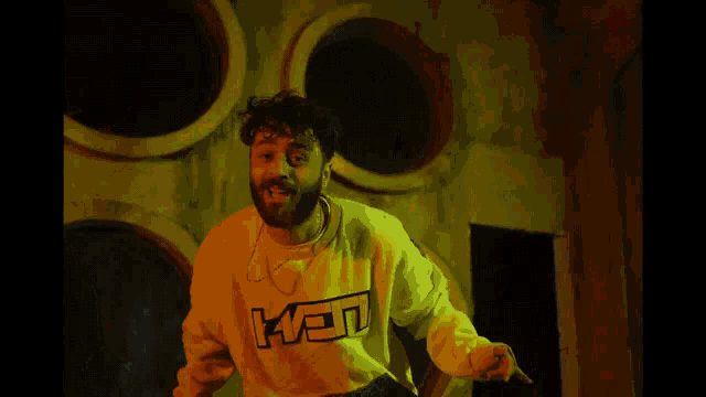 a man with a beard wears a yellow sweatshirt with the word ken on it