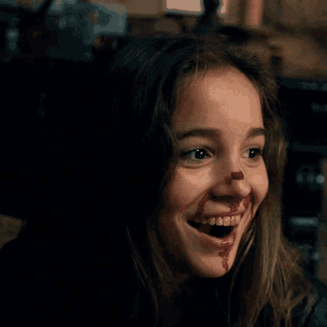 a girl with blood on her face is smiling with her mouth open