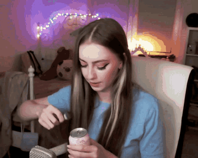 a woman in a blue shirt holds a can of soda