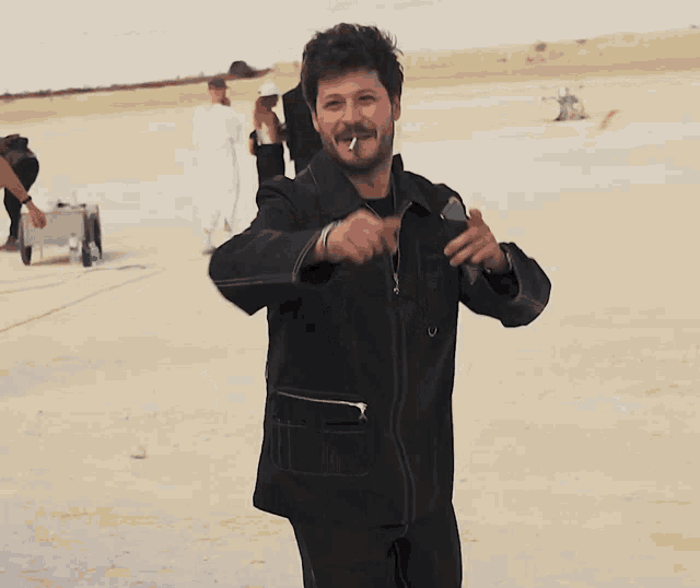 a man in a black jacket smoking a cigarette in a desert