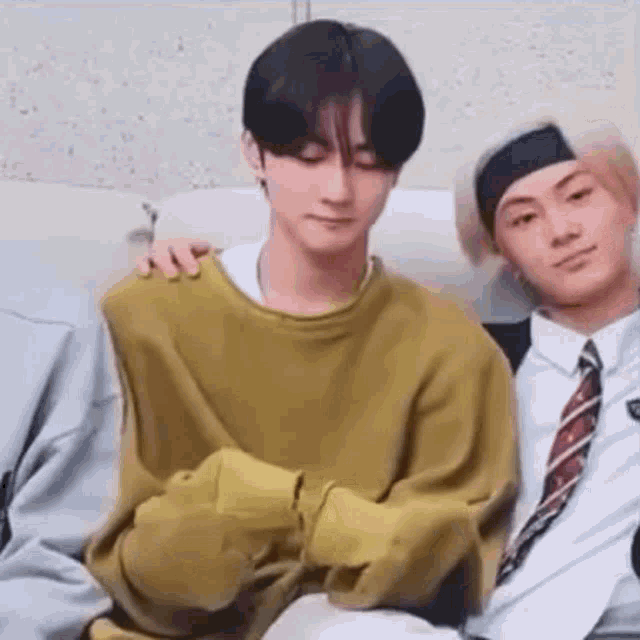 a group of young men are sitting on a couch . one of the men is wearing a yellow sweater and a tie .