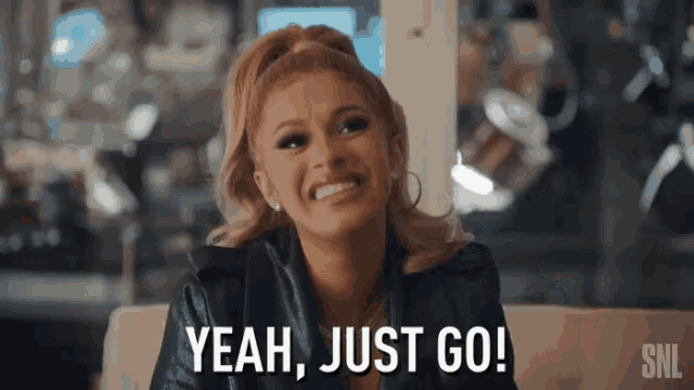 a woman is sitting on a couch and smiling and saying `` yeah , just go ! ''