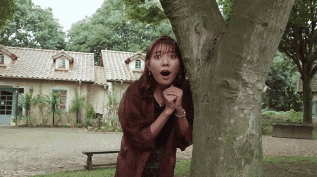 a woman is peeking out from behind a tree with her mouth open