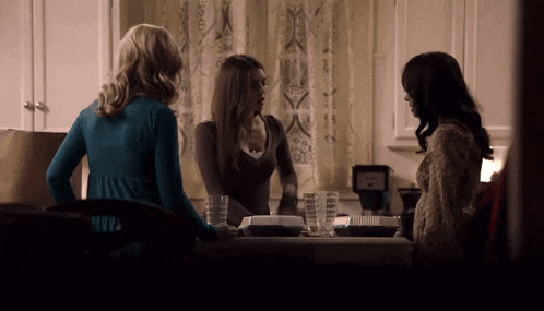 three women are standing in a kitchen with a coffee maker on the counter
