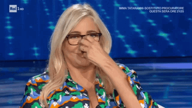 a woman wearing glasses and a colorful shirt is covering her nose with her hand