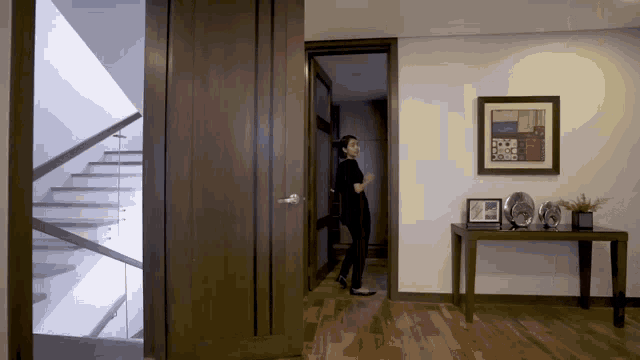a woman standing in a hallway with a picture on the wall above her