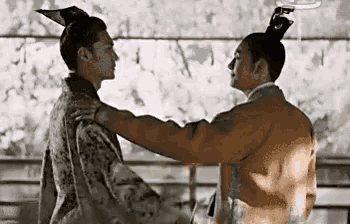 two men in ancient costumes are hugging each other in a room .