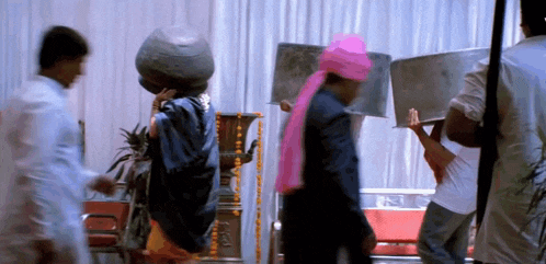 a man wearing a pink turban is carrying a large bucket on his head