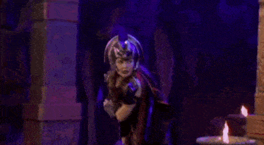 a woman in a red costume is standing in front of a purple candle .