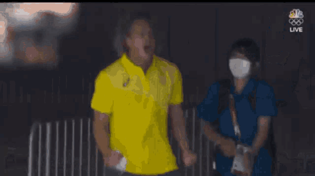 a man in a yellow shirt is standing in front of a fence .