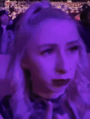 a woman with a choker around her neck is making a funny face while sitting in a crowd .
