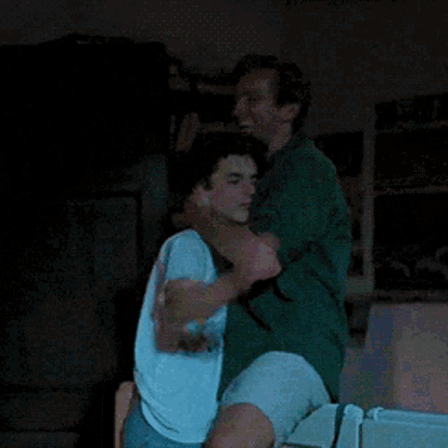a man in a white shirt is hugging another man