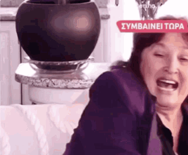 a woman in a purple jacket is sitting on a couch and laughing .