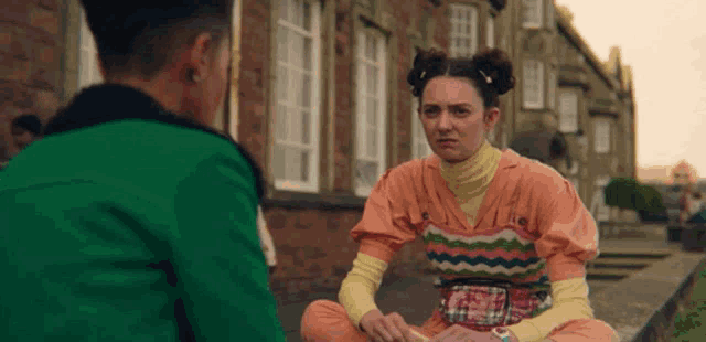 a woman in a colorful outfit is sitting in front of a man in a green jacket .