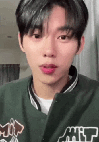 a young man wearing a green jacket and a white shirt is making a funny face .