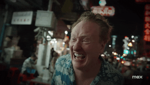 a man is laughing in front of a sign that says max on it