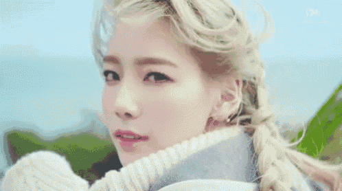 a woman with blonde hair is wearing a white sweater and a braid .