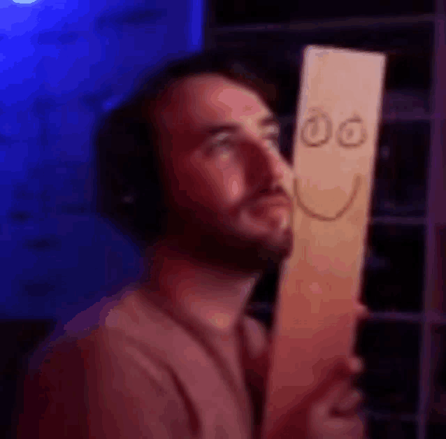 a man is holding a wooden sign with a smiley face drawn on it .