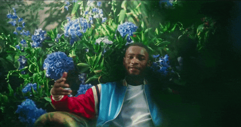 a man in a blue jacket is surrounded by purple flowers