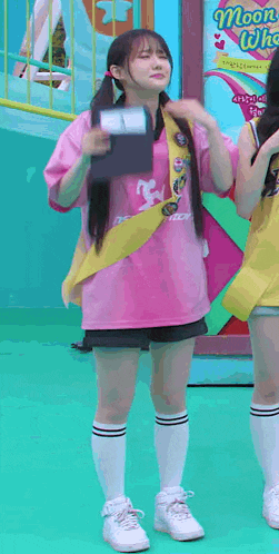 a girl in a pink shirt and white shoes is standing next to another girl in a yellow shirt .