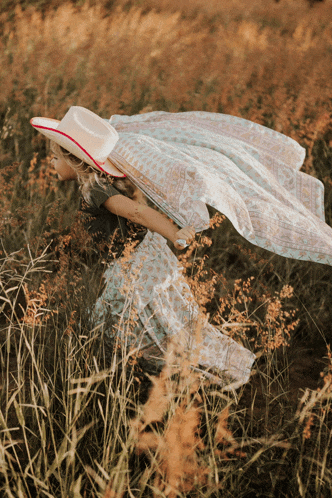 a woman wearing a white hat and a long skirt is running through a field