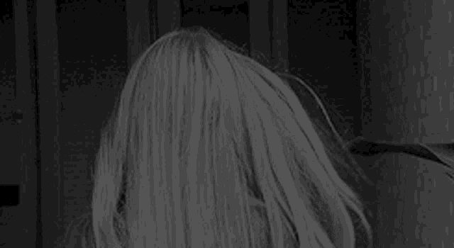 a woman with long blonde hair is standing in a dark room .