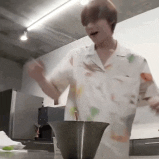 a man in a white shirt is standing in a kitchen next to a bowl .