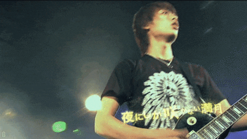 a man playing a guitar with a shirt that says ' 夜 に ' on it