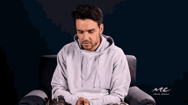 a man in a white hoodie is sitting in a chair with a mc logo in the background