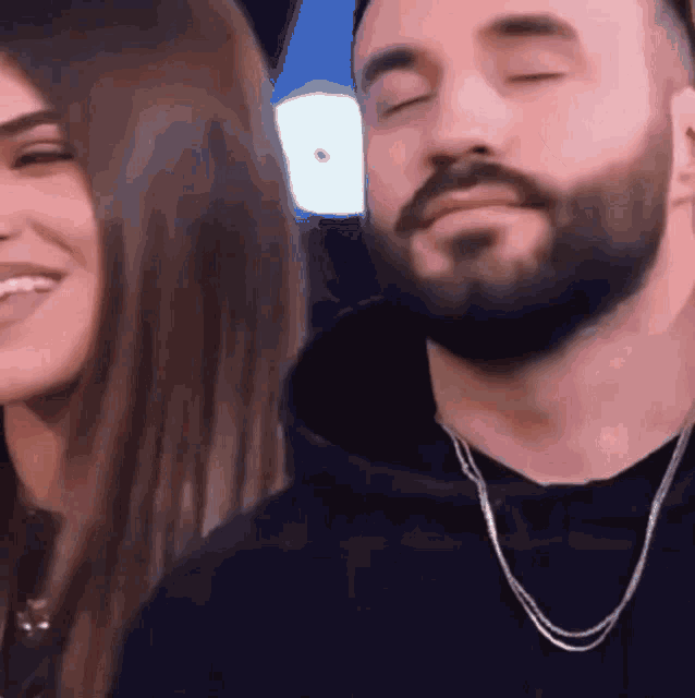 a man with a beard is standing next to a smiling woman with her eyes closed