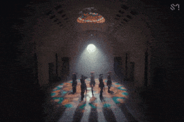 a group of people are dancing in a dark room with a light shining through the ceiling