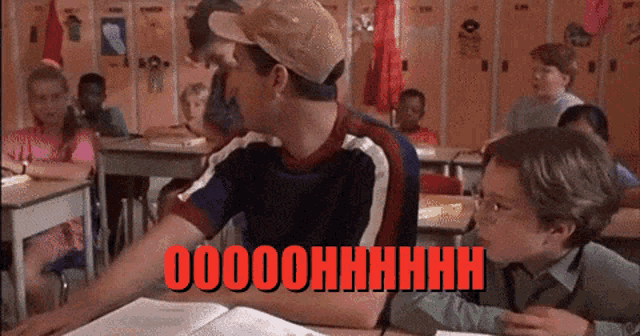a man in a baseball cap is sitting at a desk in a classroom with the words oooohhhh written on the screen