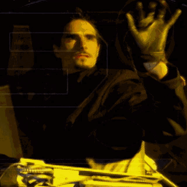 a man in a black jacket holds up his hand in a dark room