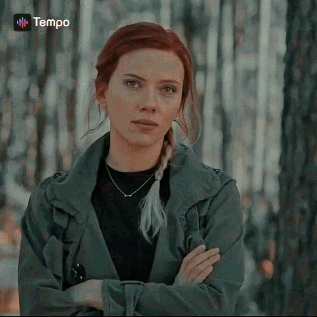 a woman in a trench coat with her arms crossed looks at the camera