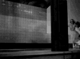 a black and white photo of a woman in a white dress standing in front of a wall .