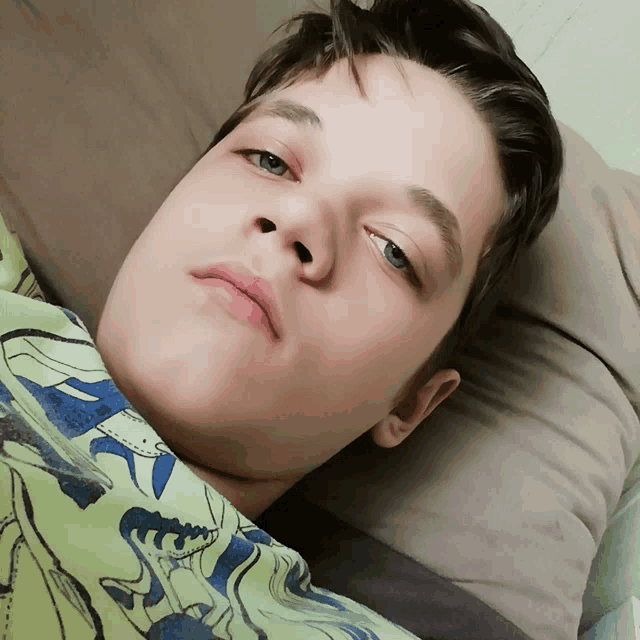 a young boy wearing a dinosaur shirt is laying on a bed