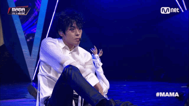 a man in a white shirt is sitting on a stage in front of a mnet banner