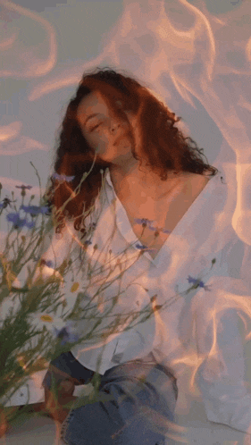 a woman in a white shirt is surrounded by flowers and fire