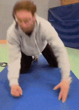 a man is kneeling on a blue mat with his hands on the mat