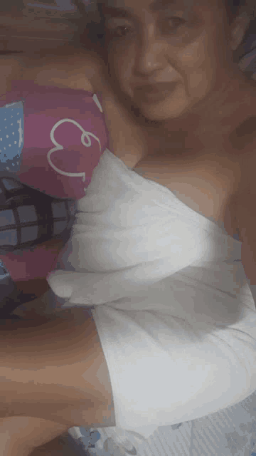 a woman wrapped in a white towel is laying on a bed with a pillow with a heart on it