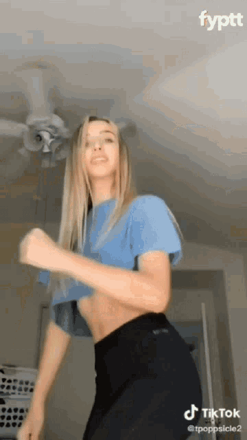 a woman is dancing in a room with a ceiling fan behind her .