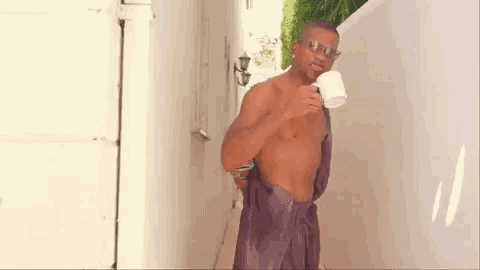 a shirtless man is holding a cup of coffee while standing next to a white wall .