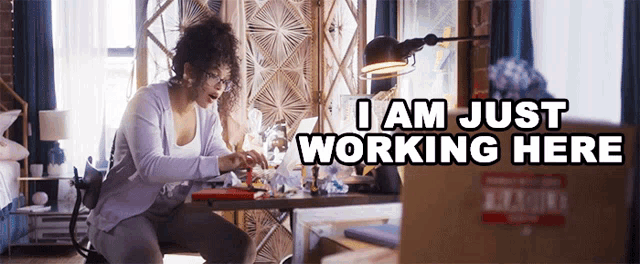 a woman sits at a desk with a laptop and the words i am just working here